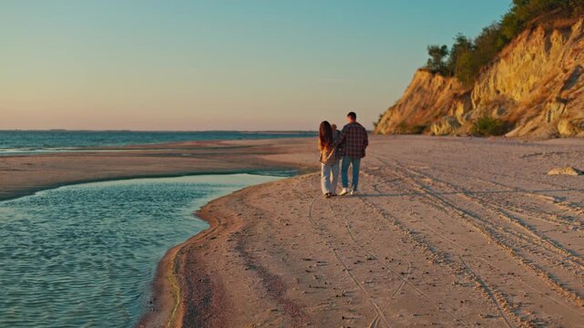 Two beachgoers stroll beside a winding tidal channel beneath sunlit coastal cliffs