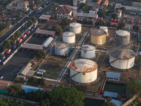 Aerial view of PT Pertamina Terminal BBM Sanggaran featuring large cylindrical fuel storage tanks, industrial piping, and tanker trucks in Kecamatan Denpasar Selatan, Bali, Indonesia.
