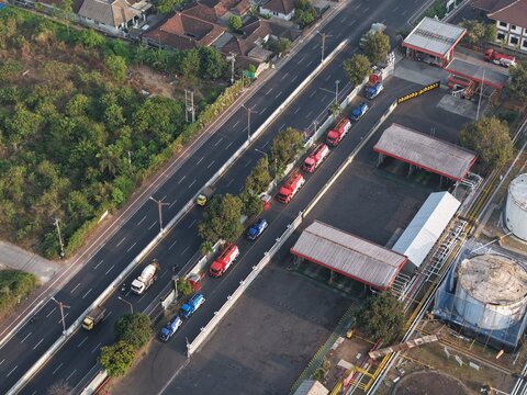 Aerial view of PT Pertamina Terminal BBM Sanggaran with fuel tanker trucks in a queue along the road and large storage tanks in Kecamatan Denpasar Selatan, Bali, Indonesia.