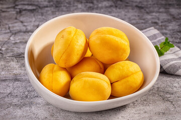 Grey stone countertop holding white ceramic bowl filled with ripe yellow shalakh apricots and green mint leaf © Andrei Starostin
