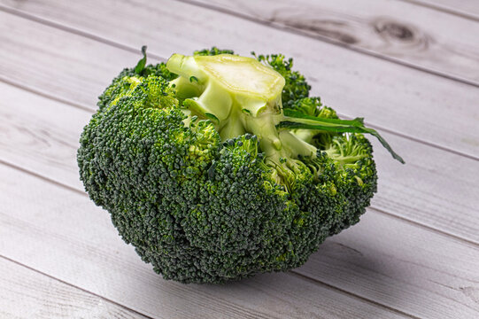 Broccoli head resting on weathered wooden tabletop showing dense green florets and thick pale stalk with detailed texture