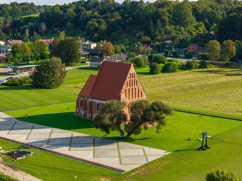 Aerial view of the historic red-brick Church of St. John the Baptist in Zapyskis, surrounded by a green lawn, a large tree, and a geometric paved area, Zapyskis, Kaunas County, Lithuania.