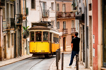 Narrow street in Lisbon with man and yellow tram, Portugal, everyday life on streets Portuguese city with people. © Tomasz
