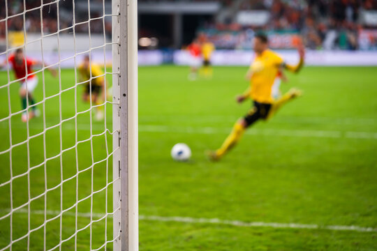Football goal post and  net with a blurred soccer player in yellow kit shooting a penalty kick