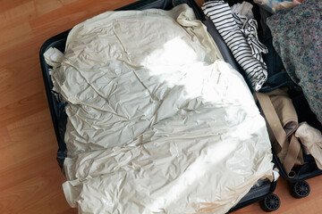 open suitcase packed with clothes and vacuum storage bags top view, both halves filled with folded garments on a wooden floor concept of travel, vacation, packing © Lana Pietukhova