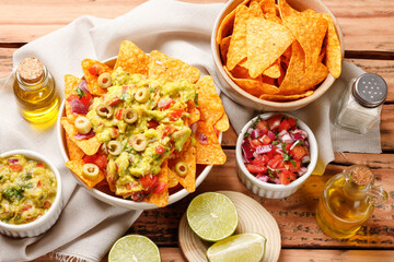 Mexican nachos tortilla chips in a ceramic bowl, topped with guacamole, chopped tomatoes, and green...
