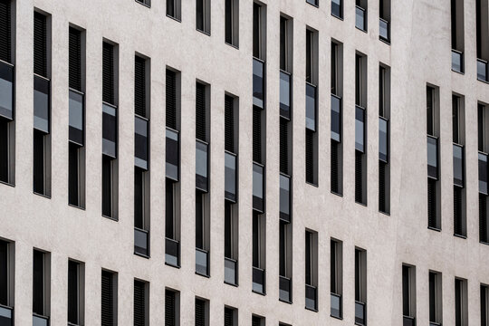 Long narrow windows form an irregular repeating pattern across a pale office facade in an abstract study of vertical geometry and modern building design