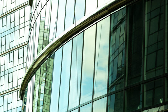 Curved green tinted glass facade with reflections of neighboring buildings creates flowing architectural lines and a layered abstract pattern on a modern office tower