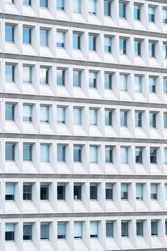 White office building facade with repeated recessed square windows creates a rhythmic geometric pattern of light and shadow across contemporary urban architecture