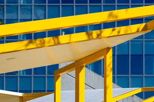 Bright yellow metal beams and canopy supports stand against a blue glass building facade creating an abstract contrast of color and geometry in contemporary architecture
