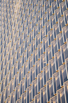 Repeating angular fins and windows across a tall building facade in warm side light creating a textured geometric architectural pattern with strong vertical rhythm