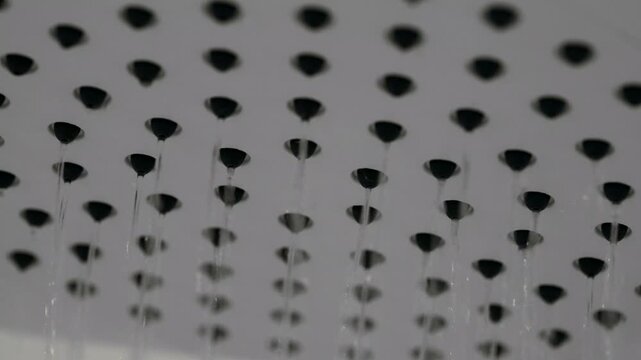 Close up shot of a hotel shower head being turned on and pouring water