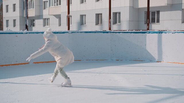 Someone glides across a sunlit ice rink. Their white coat flutters with each movement. Long shadows stretch across the smooth surface. The rink feels bright, open, and peaceful