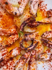 Traditional Galician-style octopus served with sweet potato, olive oil, paprika and herbs on a plate © Марина Гудзь