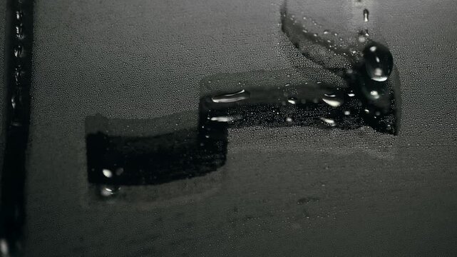 Water droplets dripping down a steamy mirror in dull bathroom light