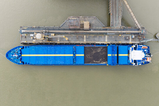 Aerial view of a blue cargo ship docked at a terminal with bulk material in its hold in the United Kingdom.