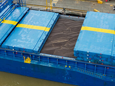Aerial view of a cargo ship with open hatches filled with dark bulk cargo, featuring a blue hull and yellow deck markings, United Kingdom.