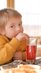 Child boy with blonde hair baby drinking lemonade in cafe. 3 years old kid drinks red juice from glasses through straws. Boy toddler in a restaurant. Closeup natural emotion vintage portrait. © Marina Demidiuk