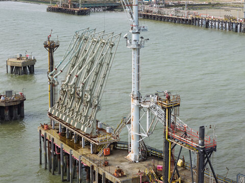 Aerial view of an industrial oil loading jetty with multiple loading arms, a tall mast, and offshore platforms in the water in the United Kingdom.
