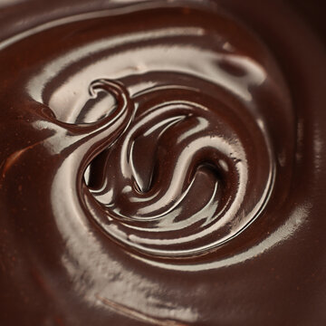 Glossy dark chocolate cream with swirling ridges and reflective highlights in a close up abstract food texture composition