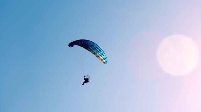 paraglider flying in blue sky with sun flare during bright summer day
