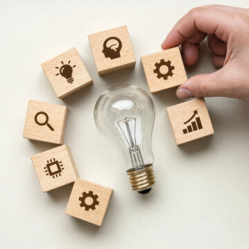 Hand putting wooden blocks with business icons around a glass light bulb