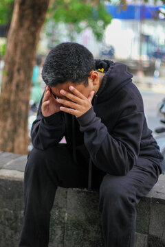 Asian man suffering from a headache, holding his head and feeling intense pain, against a bokeh background.