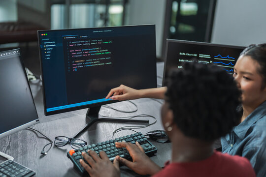 Over-the-shoulder view of a woman pointing at lines of code on a monitor as her teammate types, working together to fix a software bug.
