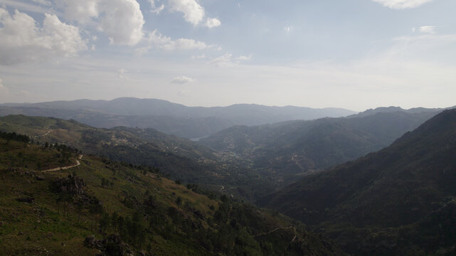 Aerial view of Peneda-Geres National Park featuring rolling mountains, a winding dirt road, and a valley under a hazy sky in Portugal.