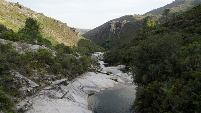 Aerial view of the rocky pools of Pocos Verdes surrounded by lush green hills and a winding stream in Cabril, Vila Real, Portugal.