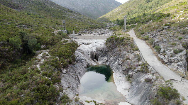 Aerial view of the Pocos Verdes natural rock pool surrounded by rugged mountains, lush green vegetation, and stone structures in Cabril, Vila Real, Portugal.