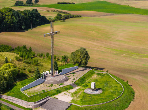 Aerial view of the Pope's Altar monument featuring a large metal cross, surrounded by green fields and trees in Pelplin, Pomeranian Voivodeship, Poland.