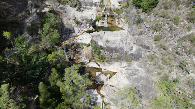 Aerial view of Cascatas de Fecha de Barjas featuring cascading waterfalls, natural rock pools, surrounding lush forest, and rugged granite terrain in Salamonde, Braga, Portugal.