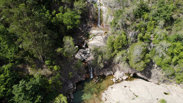 Aerial view of Cascatas de Fecha de Barjas, featuring cascading waterfalls flowing over rocky terrain into a clear pool, surrounded by lush forest in Salamonde, Braga, Portugal.