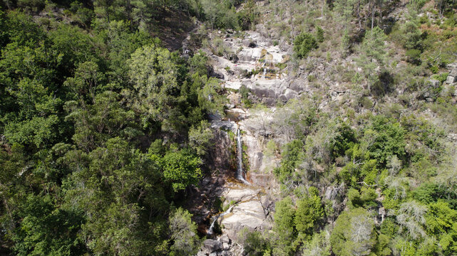 Aerial view of Cascatas de Fecha de Barjas waterfall cascading down rocky cliffs surrounded by lush green forest in Salamonde, Braga, Portugal.