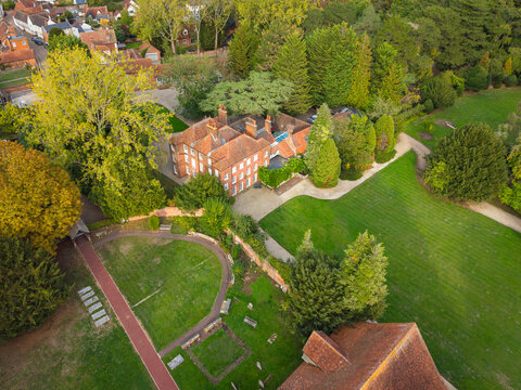 Interesting drop view of a large Manor House seen within lush lawns and woods in the rural village of Blackmore, Essex, UK. A cemetery is on the left side of the image.
