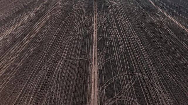 Aerial drone view of cultivated agricultural field with dark brown soil, parallel furrows and intersecting tractor tracks. Abstract geometric patterns reveal farmland texture in rural Germany autumn