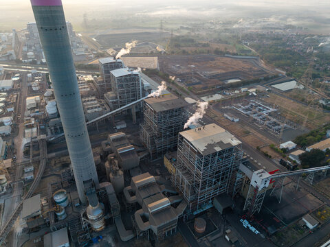 Aerial view of PLTU Tanjung Jati power plant with its tall chimney, industrial structures, and steam rising from the cooling towers in Kecamatan Kembang, Jawa Tengah, Indonesia.