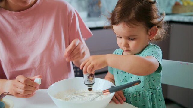 Little girl adds flavor to mixing bowl with curiosity. Mother guides her gently, smiling warmly. Child focuses intently on the task with delight. Perfect for family cooking or parenting content