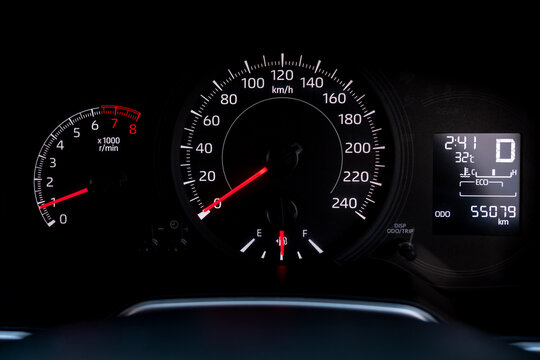 Close up of modern car dashboard speedometer and tachometer gauge panel displaying fuel level, engine temperature, mileage odometer, gear indicator and parking brake warning light.