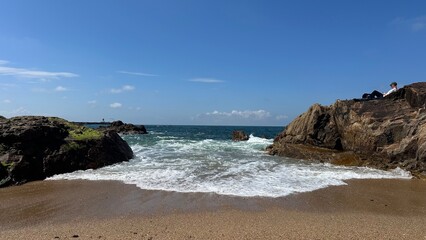 Petite crique de sable entre les rochers et vagues écumantes © Cyril