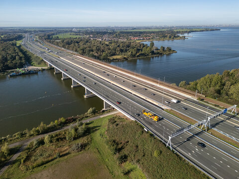 Aerial view of Hollandse Brug spanning the water with a busy highway and railway tracks running parallel through the green landscape in Naarden, Flevoland, Netherlands.
