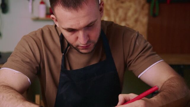 Craftsman marks wood with red pencil, focused and precise. Workshop setting suggests skilled manual labor and creativity. Ideal for DIY, craftsmanship, or artisanal project visuals