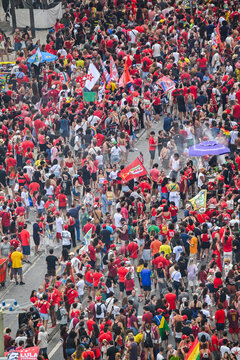 Rio de Janeiro, Brazil - 12 October 2026: Aerial view of a large crowd at a political rally in Copacabana, with supporters wearing red, carrying flags, banners, and filling the street.