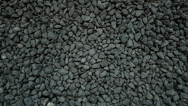 Dense top-down view of small dark grey gravel stones texture, crushed basalt rock background for landscaping or path.
