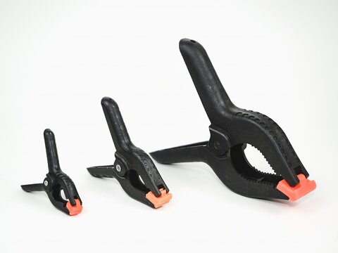Set of three black plastic spring clamps in small, medium, and large sizes with orange tips on an isolated white background