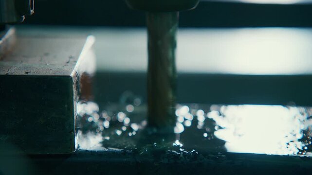 Drill bit plunges into metal block. Coolant splashes as metal shavings fly. Close-up shot reveals industrial precision. Ideal for manufacturing or machinery themes. No people, no animals