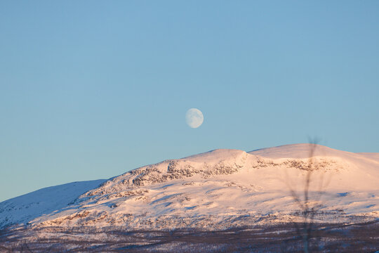 Full moon above snow covered mountains in Kiruna, Swedish Lapland, Sweden