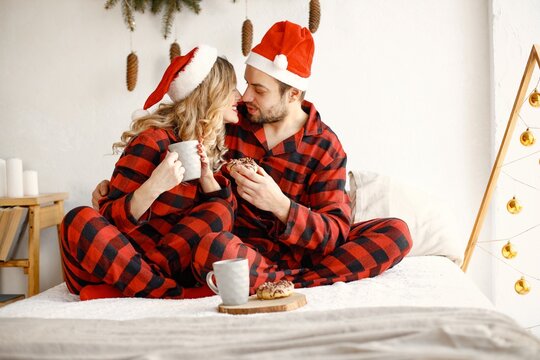 Couple wearing christmas plaid red pajamas sitting on the bed