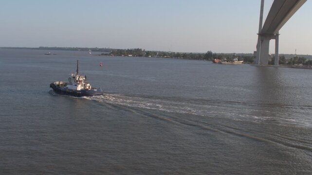 elevated video frame of an industrial tugboat heading outward and cruising through the waters of maputo bay past the suspension bridge and out to sea under daytime light